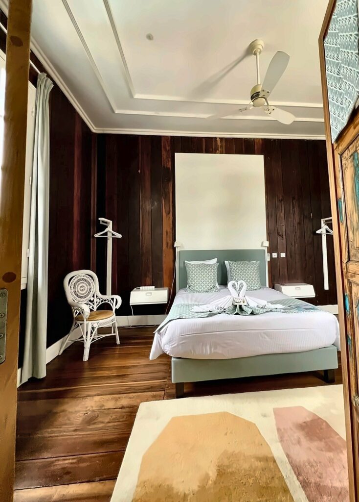 Chambre Chloé vue depuis la porte, lit queen size, boiseries anciennes et ventilateur de plafond — Villa Myriam, Saint-Pierre